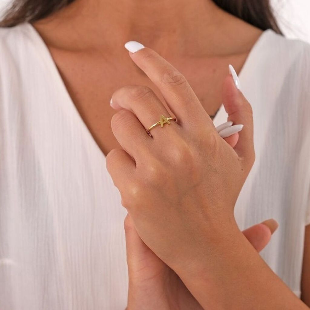 Close-up of a hand wearing a gold ring with a green stone, against a neutral background.