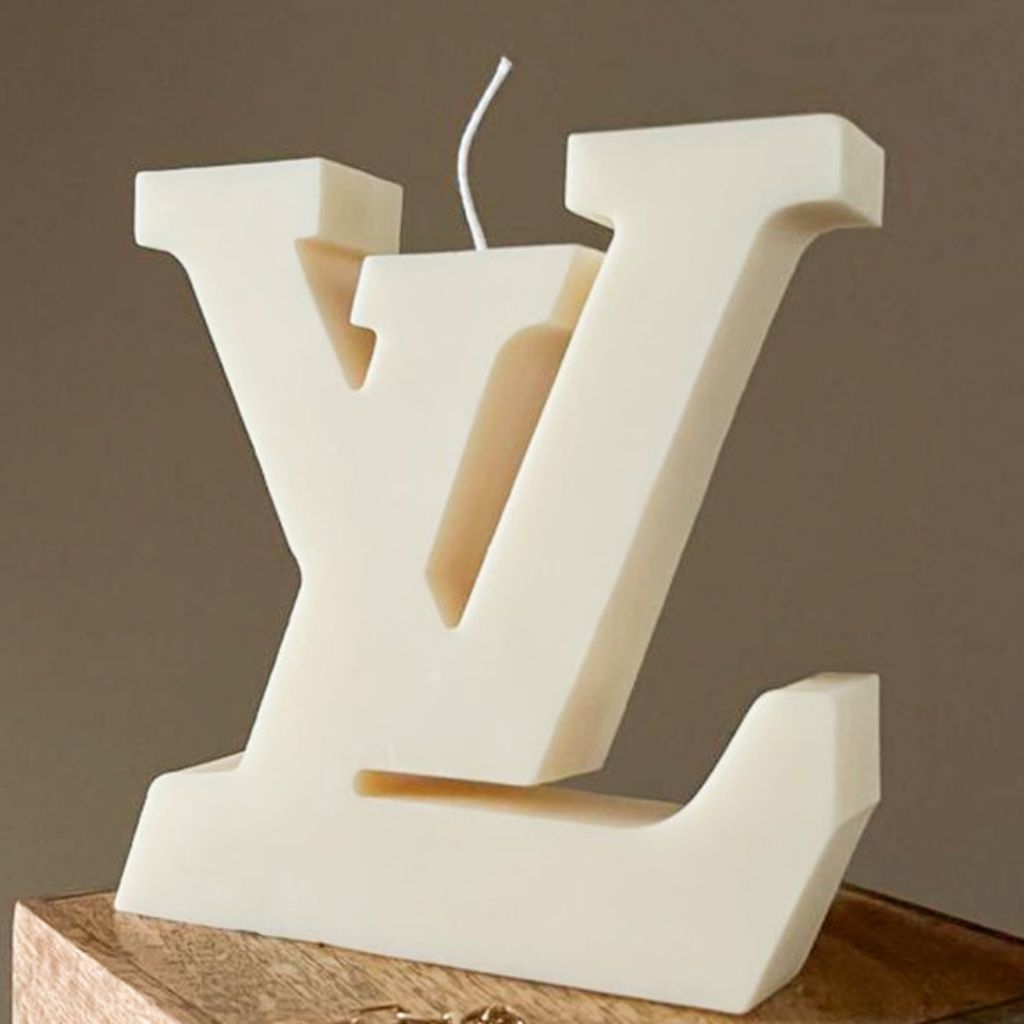 Decorative candle shaped like a large white letter 'V' on a wooden base with a brown background.