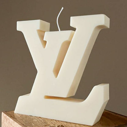 Decorative candle shaped like a large white letter 'V' on a wooden base with a brown background.