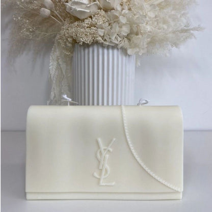White handbag with a brand logo in front of a vase with white flowers on a light background