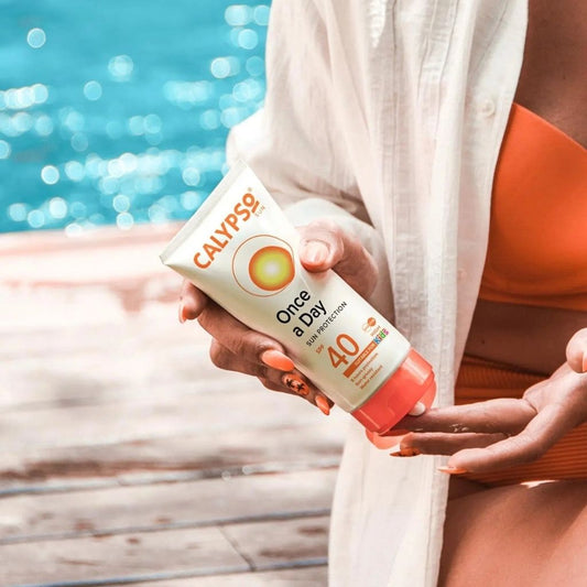 Person holding a Calypso sunscreen bottle by a pool