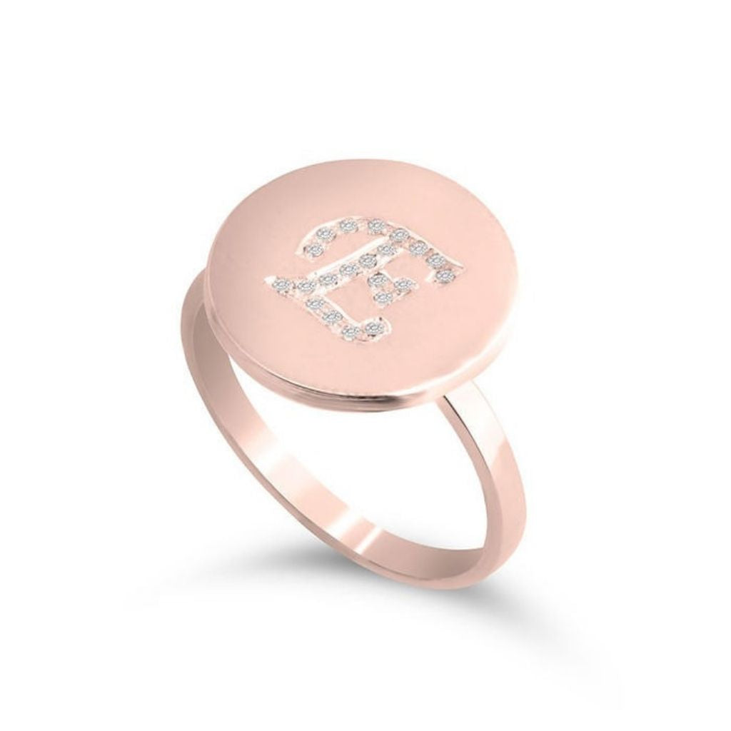 Rose gold ring with a circular pendant featuring small diamonds on a white background