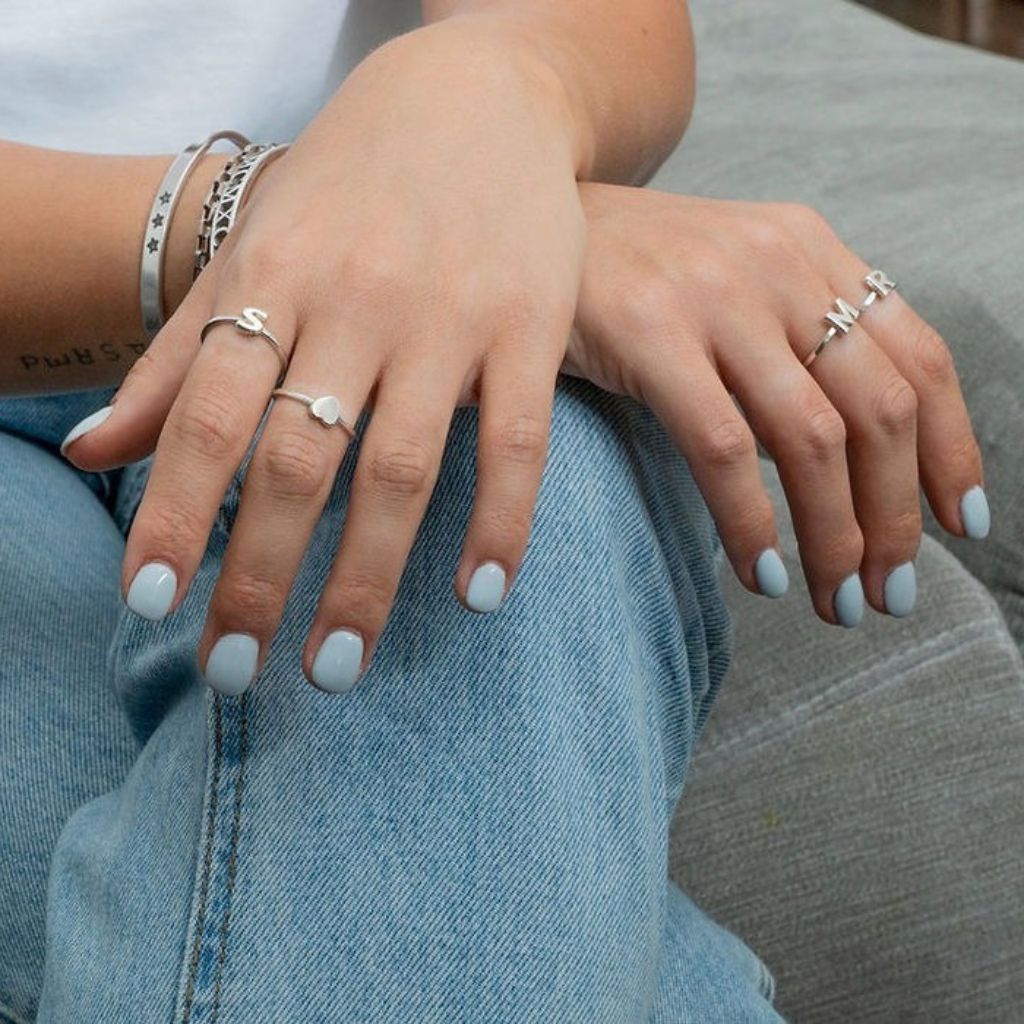 Close-up of hands with multiple rings and light blue nail polish on a denim background