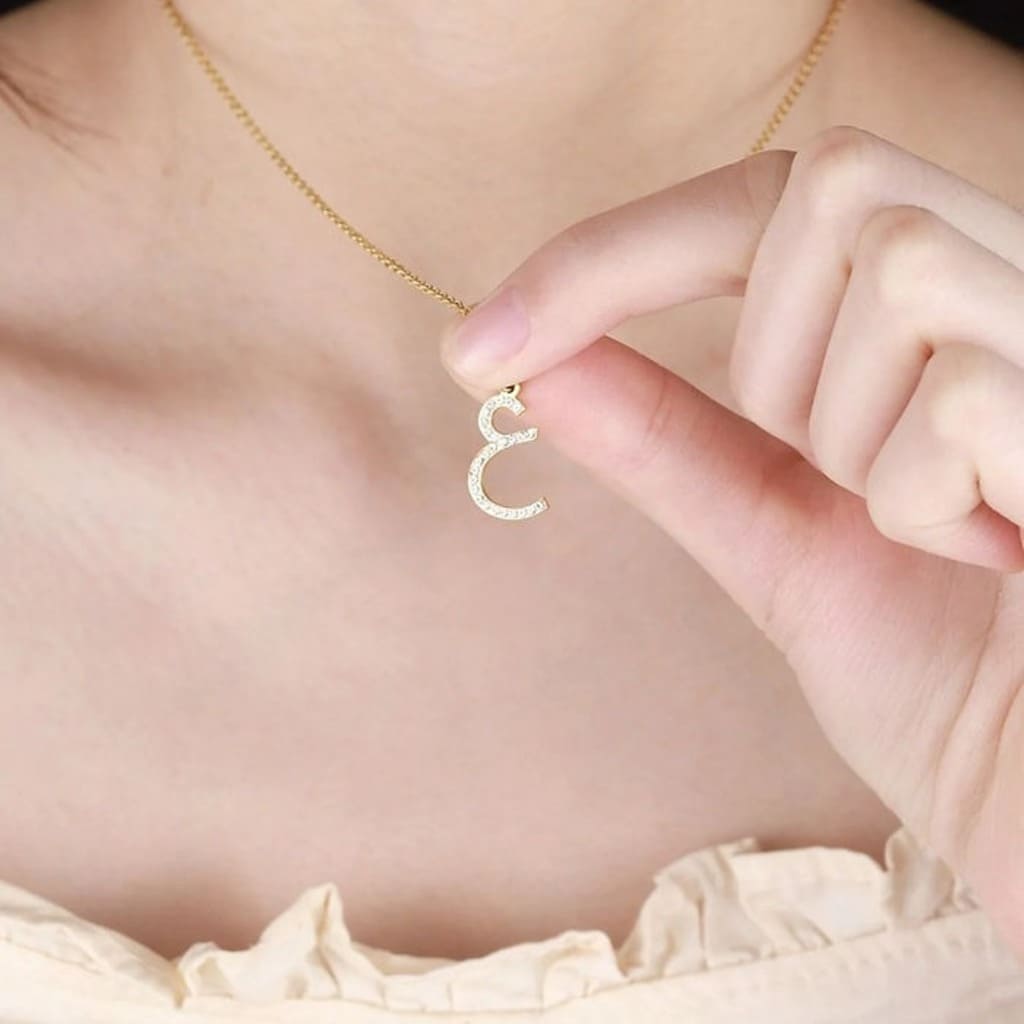 Gold necklace with a unique pendant held by a hand against a soft background