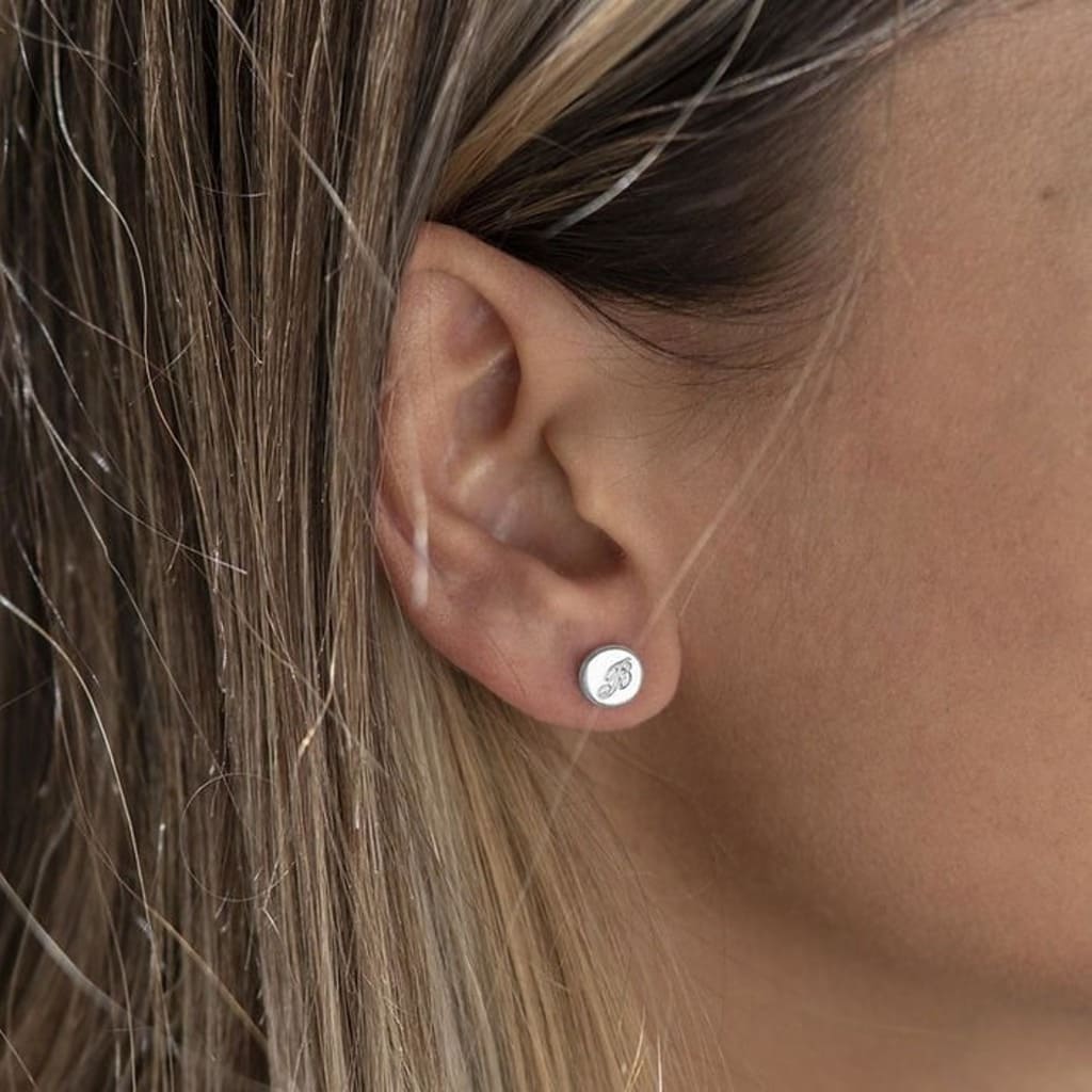 Close-up of an ear wearing a silver stud earring with hair partially covering the frame.