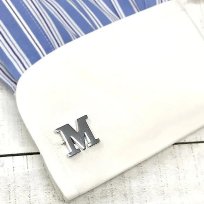 White phone case with a silver 'M' charm on a striped fabric background