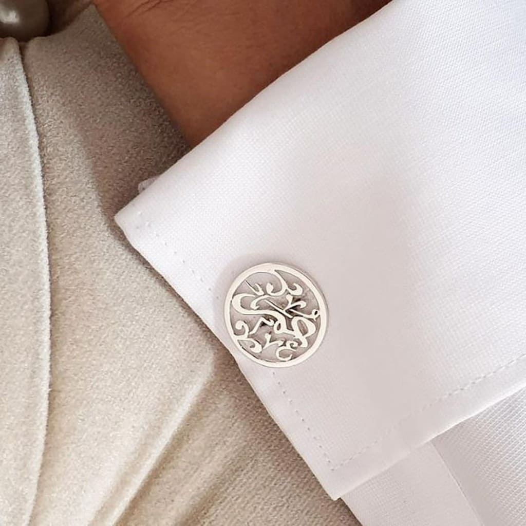 Close-up of a cufflink on a white shirt cuff with a beige jacket.