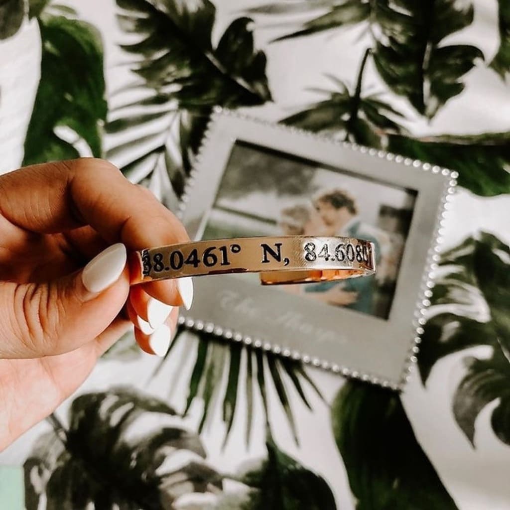 Hand holding a bracelet with coordinates against a leafy background