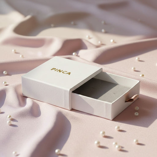 PINCA jewelry box on a pink fabric background with scattered pearls