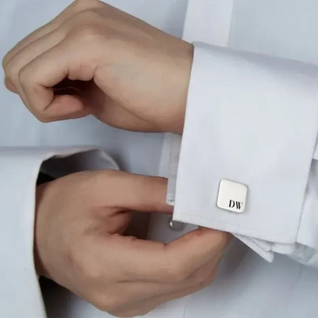 Person adjusting a cufflink on a white shirt with a visible brand logo.