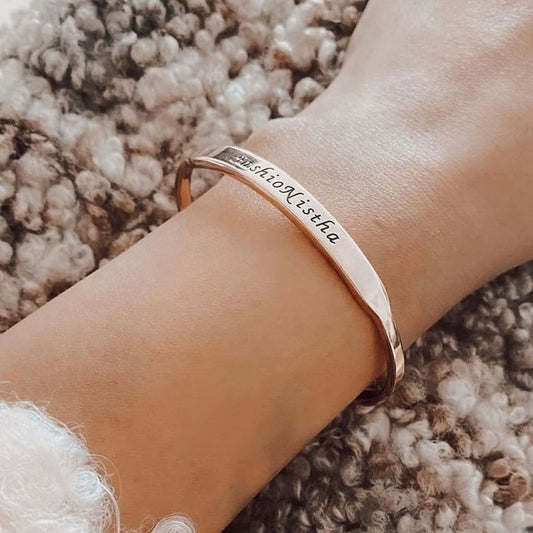 Rose gold bracelet with engraved text on a wrist against a textured background