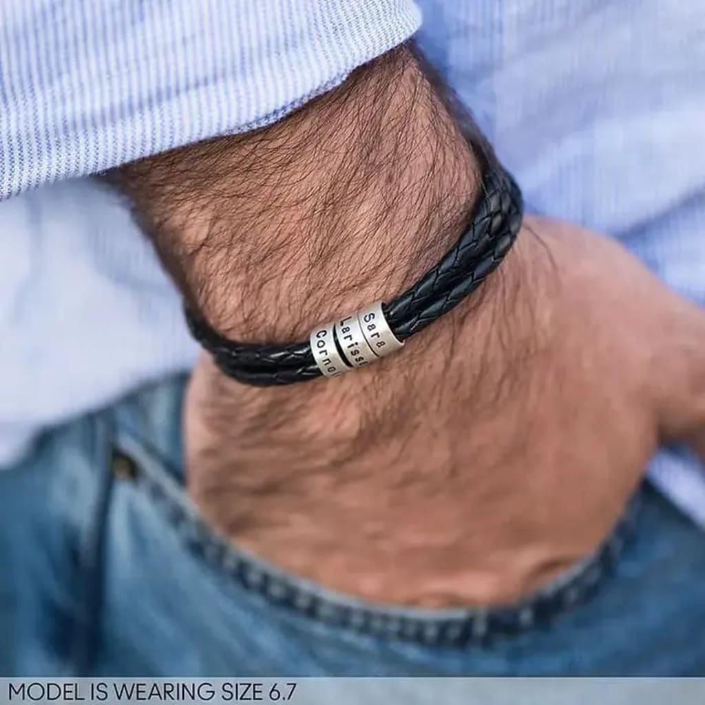 Black braided leather bracelet with metal elements on a wrist, wearing a blue shirt and jeans.