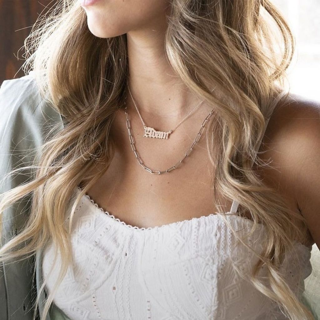 Close-up of a person wearing a delicate necklace with a nameplate.