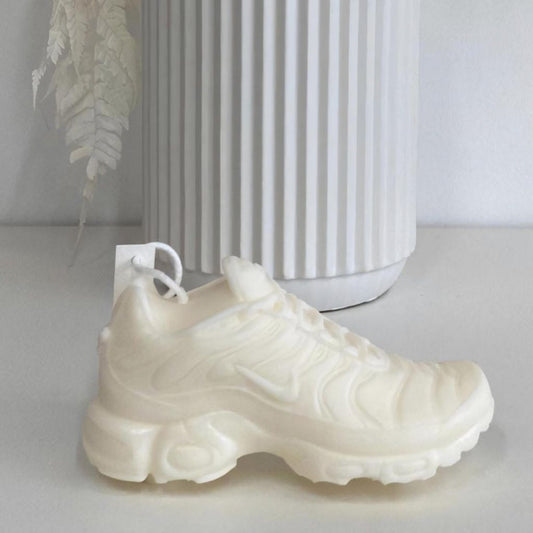 White sneaker candle on a white surface with a white vase in the background