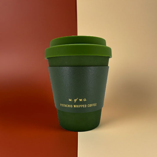 Green reusable coffee cup with a lid on a two-tone background