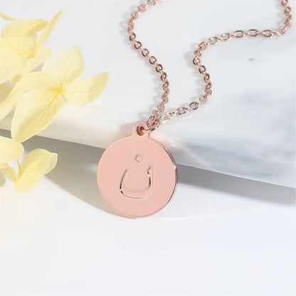 Rose gold necklace with a circular pendant on a white surface with yellow flowers.