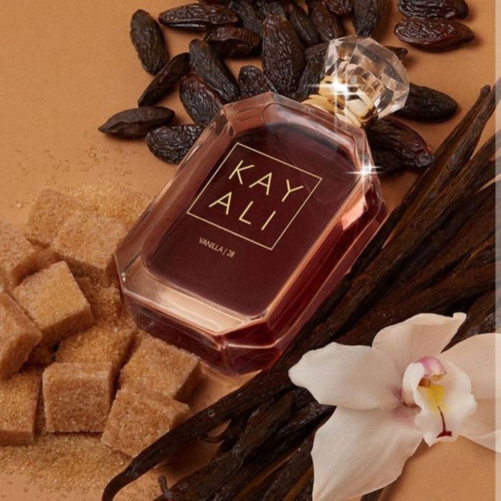 Kay Ali vanilla 28 perfume bottle surrounded by vanilla beans, sugar cubes, and an orchid on a brown background.