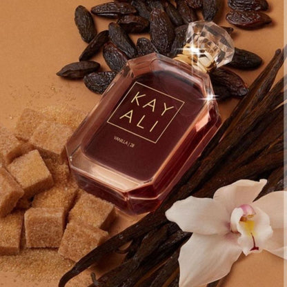 Kay Ali vanilla 28 perfume bottle surrounded by vanilla beans, sugar cubes, and an orchid on a brown background.