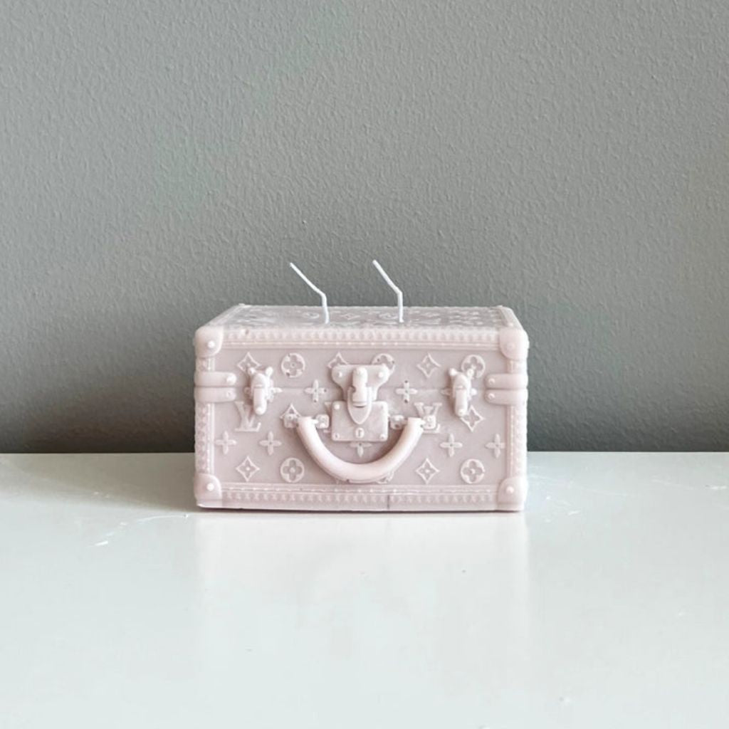 Pink suitcase-shaped candle on a white surface with a gray background