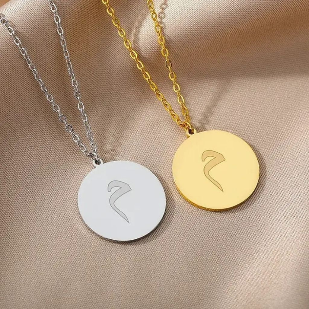 Two necklaces with circular pendants featuring Arabic calligraphy on a beige fabric background.