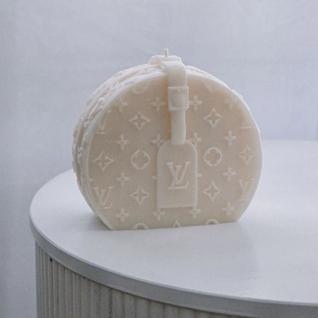 Round beige travel case with monogram pattern on a white surface