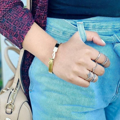 Close-up of a person's hand wearing multiple rings and a bracelet, with a blurred background.