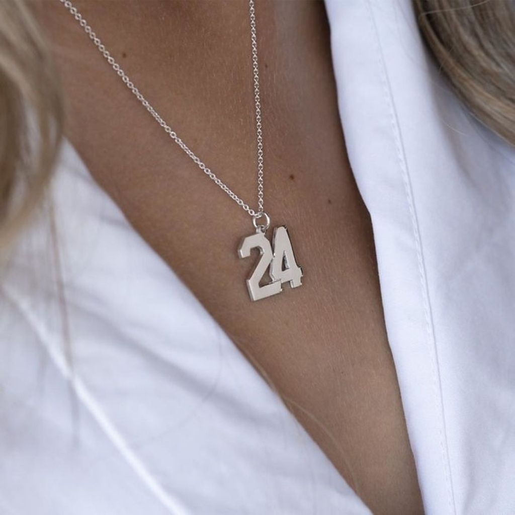 Silver necklace with the number 24 pendant worn by a person in a white shirt.
