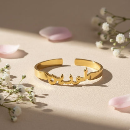 Gold bracelet with Arabic script on a beige surface with flowers