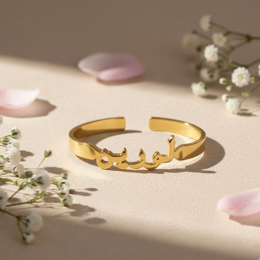 Gold bracelet with Arabic script on a beige surface with flowers