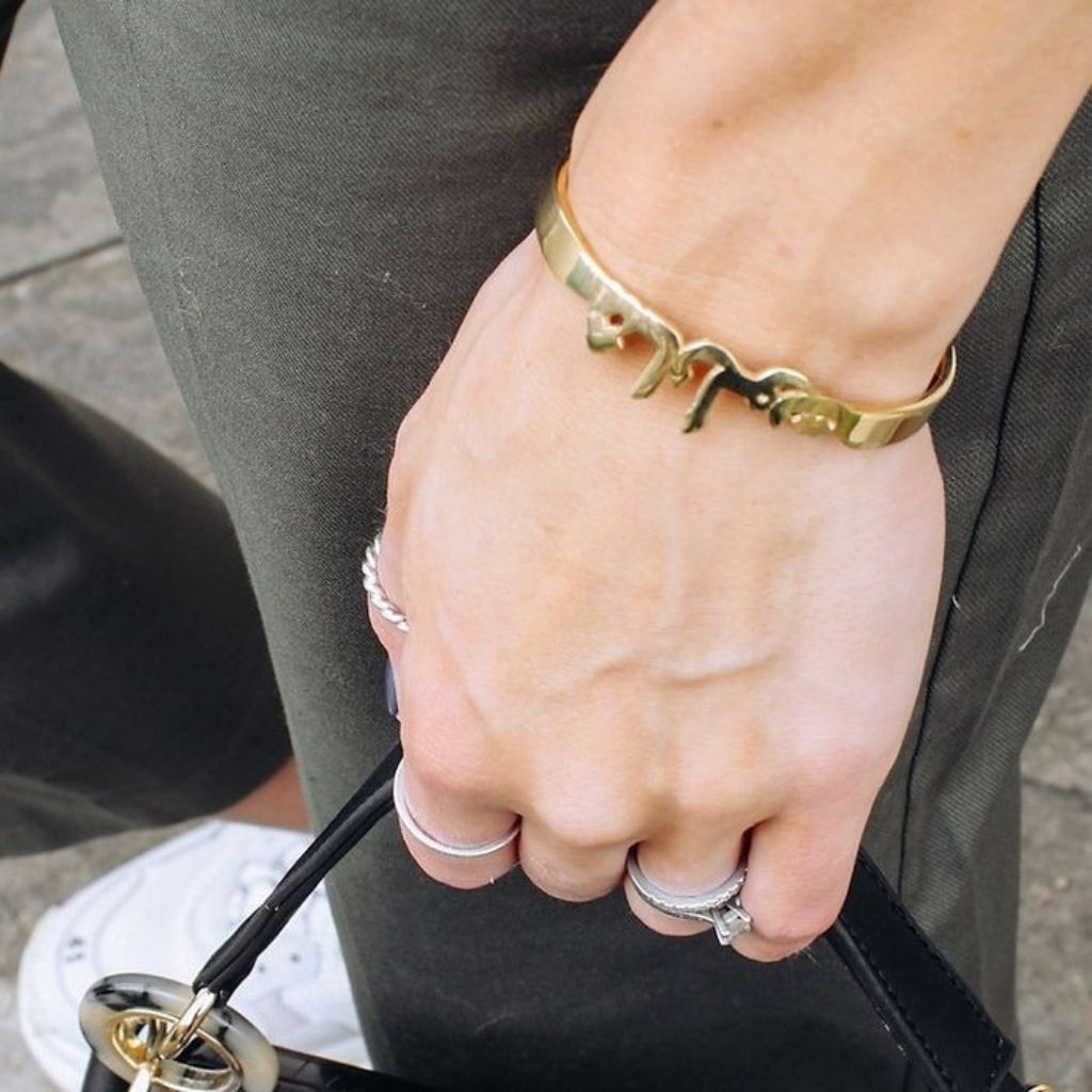 Hand wearing a gold bracelet and multiple rings on a blurred background