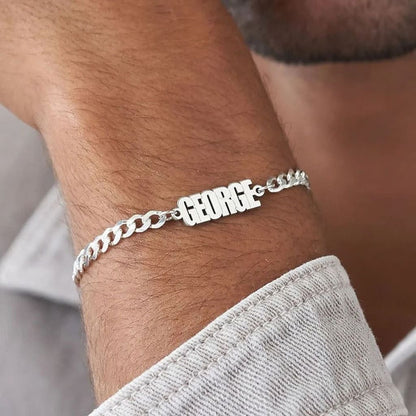 Silver bracelet with 'GEORGE' on a wrist, blurred background