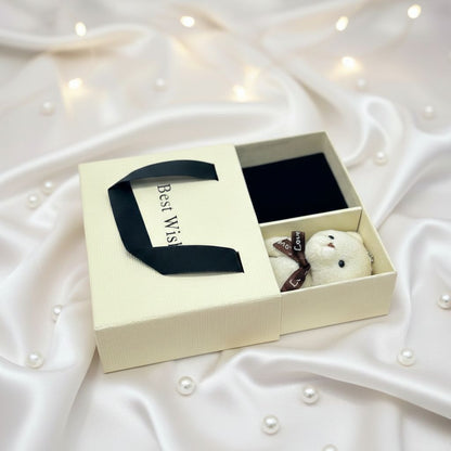 Gift set with a small teddy bear and a black ribbon in a decorative box on a white fabric background.