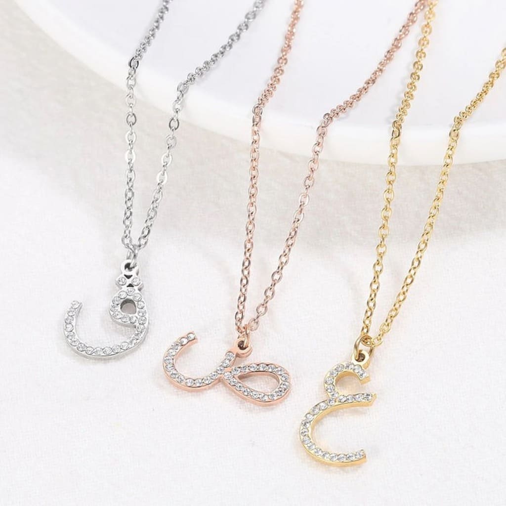 Three necklaces with letter pendants in silver, rose gold, and gold on a white background