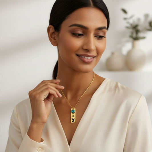 Woman wearing a gold necklace with a pendant, smiling in a neutral setting.