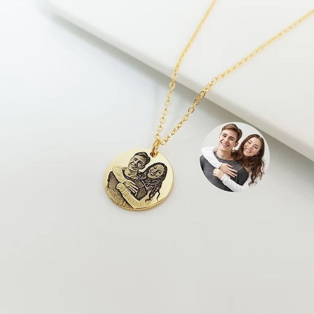 Gold necklace with a round pendant and a heart design, featuring a photo of a couple on a white surface.