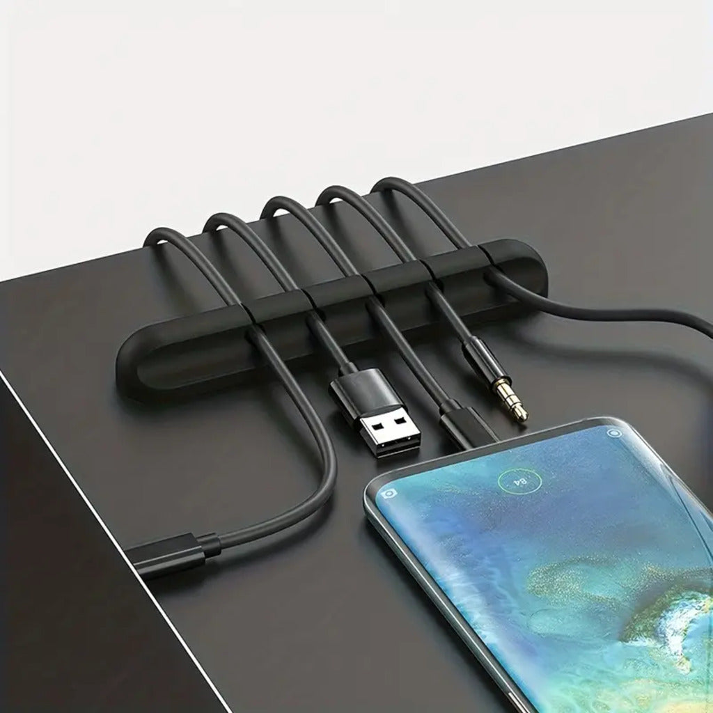 Black cable organizer with multiple cables on a dark surface, next to a smartphone.