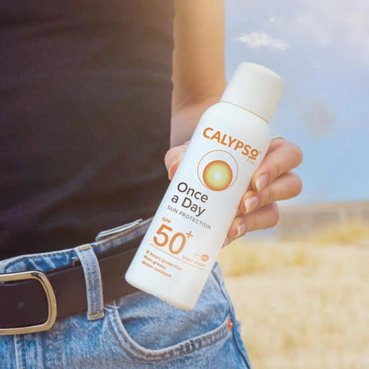 Person holding a Calypso sunscreen spray bottle with a blurred background