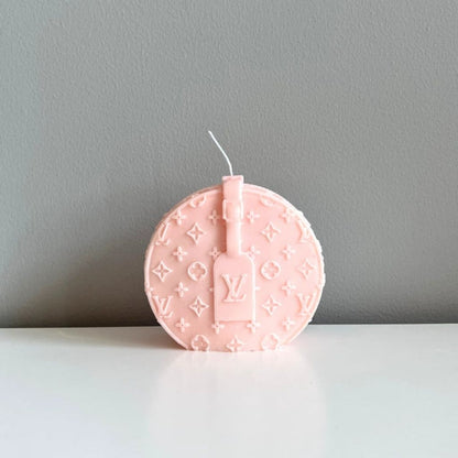 Pink round candle with a brand logo on a gray background