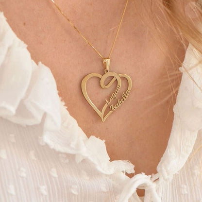 Gold heart-shaped necklace with engraved names on a person wearing a white blouse.