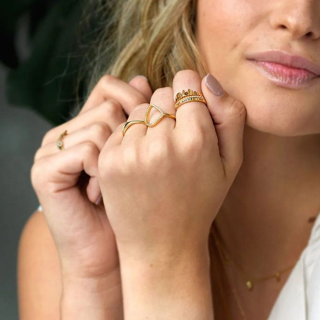 Close-up of a woman's hands wearing gold rings with a neutral background