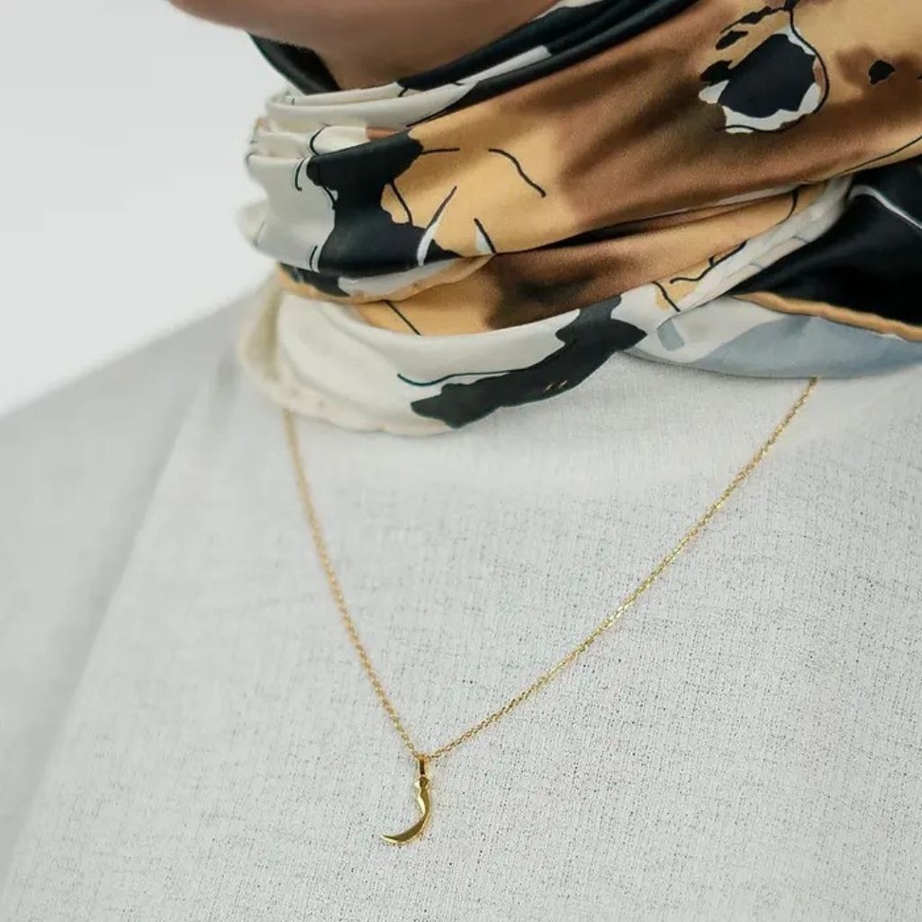 Person wearing a patterned scarf with a gold necklace on a light background
