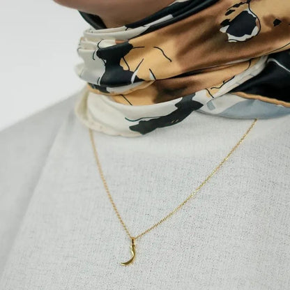 Person wearing a patterned scarf with a gold necklace on a light background