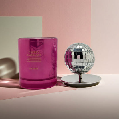 Pink candle with 'Cherry & Apricot' text next to a disco ball on a pink and beige background