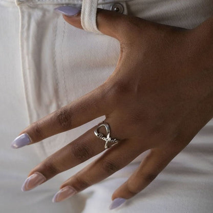 Hand wearing a silver ring with 'Bella' on a light background