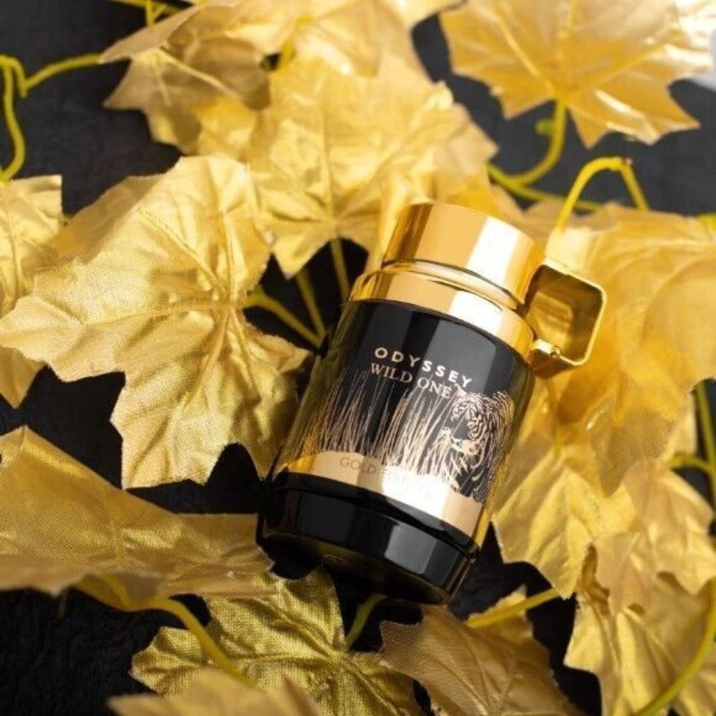 Perfume bottle labeled 'Odyssey Wild One' on a decorative background with gold leaves.