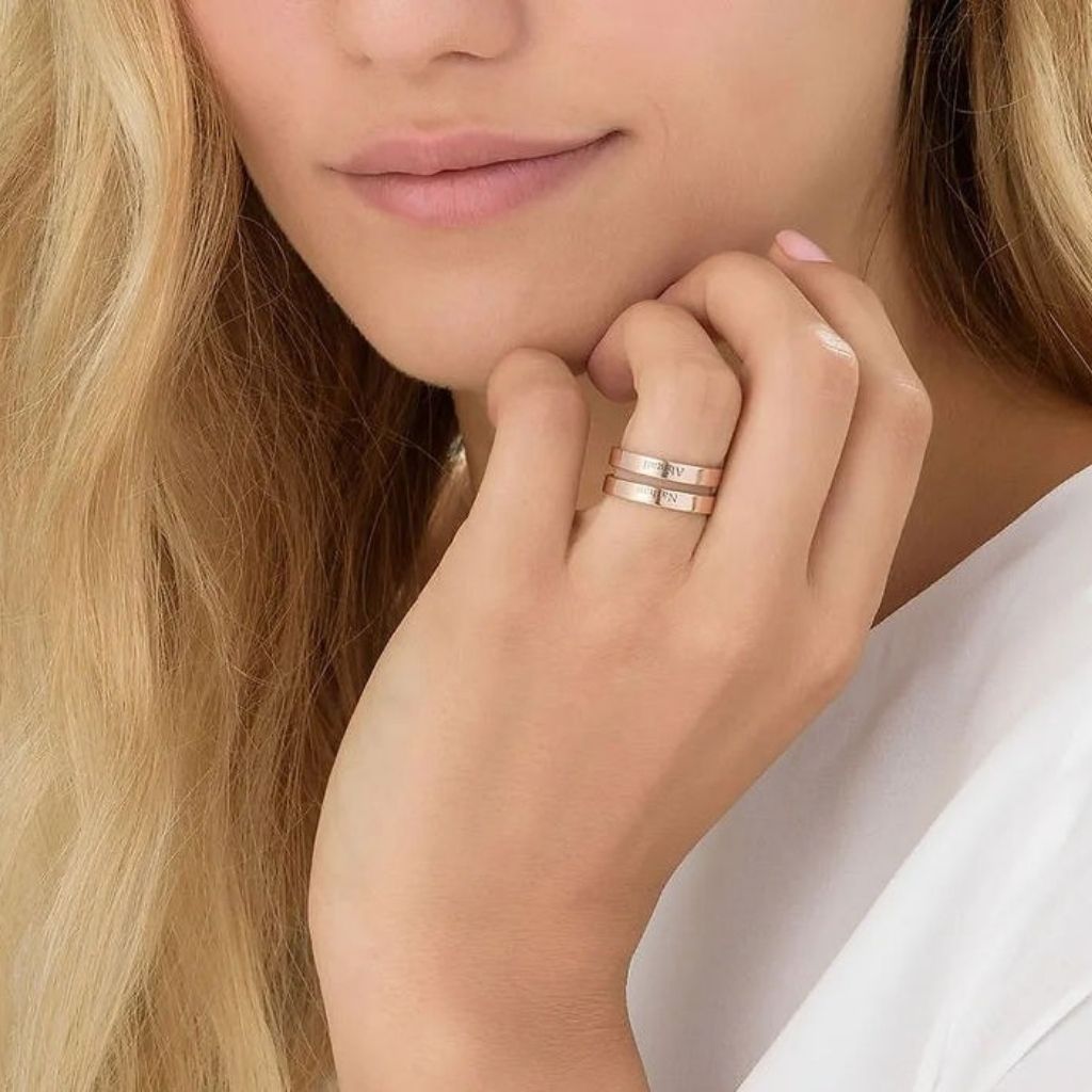 Close-up of a woman's hand wearing two gold rings with a soft focus on her face.
