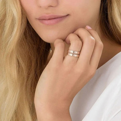 Close-up of a woman's hand wearing two gold rings with a soft focus on her face.