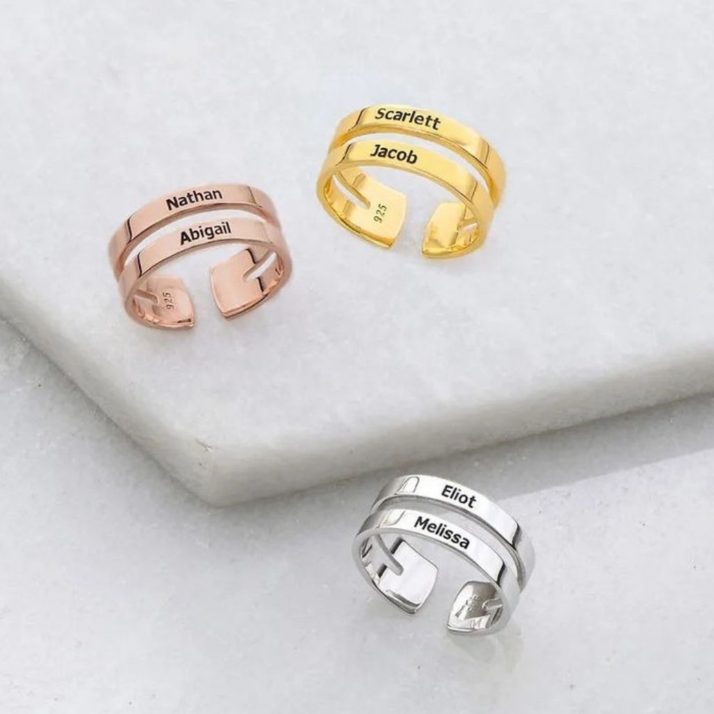 Three adjustable name rings in rose gold, gold, and silver on a light gray surface.