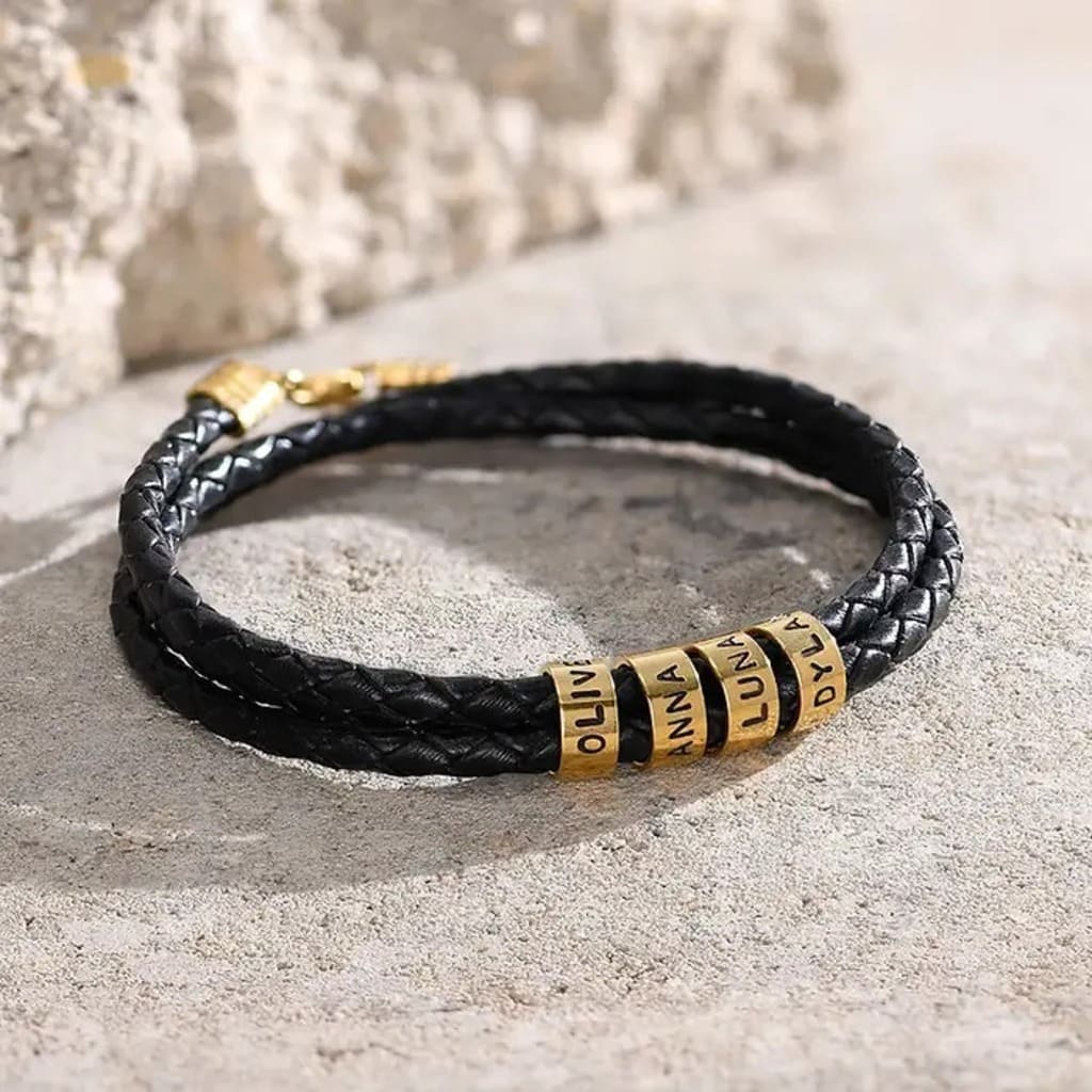 Black braided leather bracelet with gold cylindrical beads on a textured surface