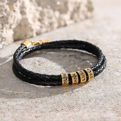 Black braided leather bracelet with gold cylindrical beads on a textured surface